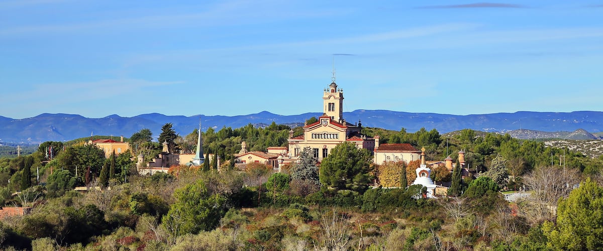 A historic building with a bell tower, surrounded by lush greenery and mountains in the background.