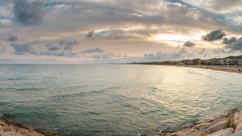 A coastal cityscape with a beach, rocky shoreline, and buildings in the background.