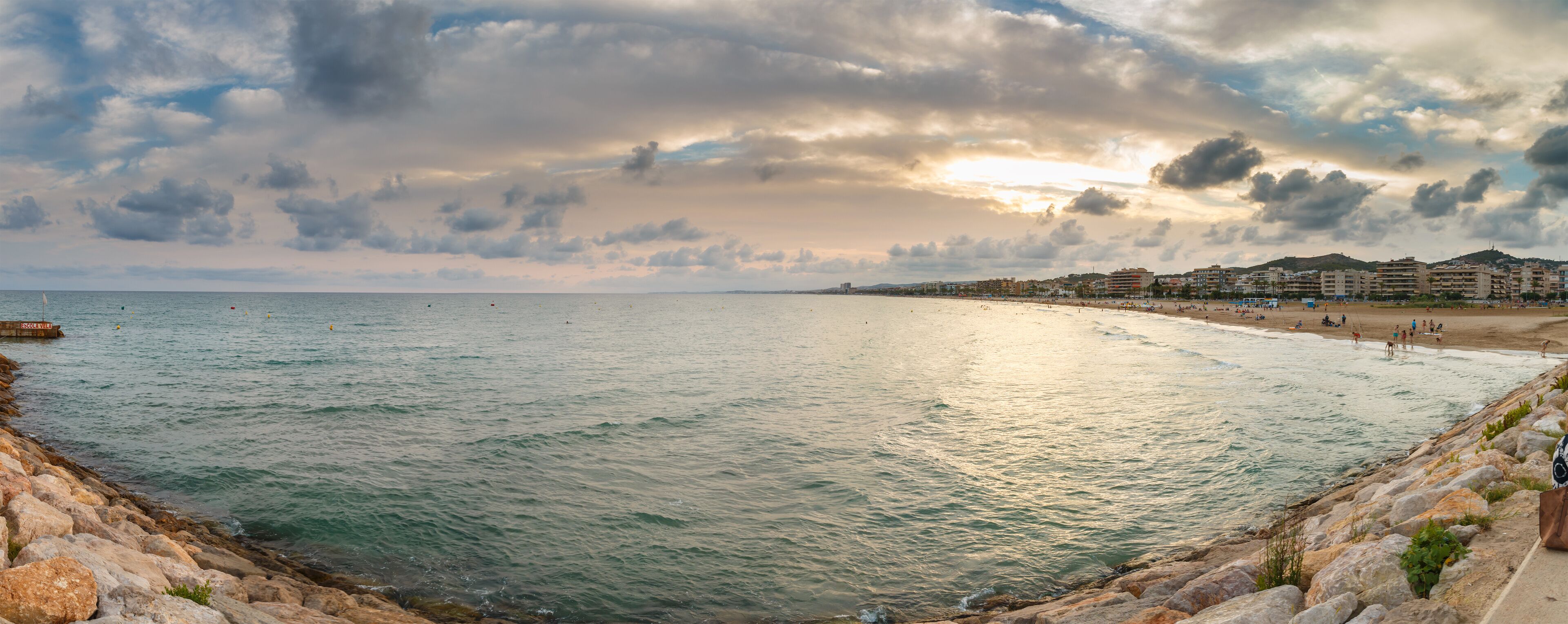 A coastal cityscape with a beach, rocky shoreline, and buildings in the background.