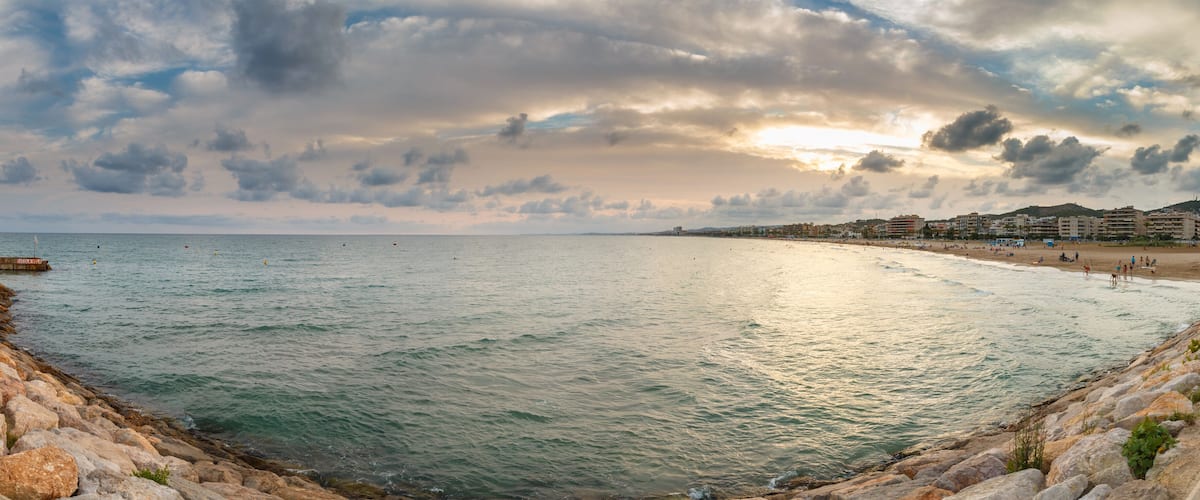 A coastal cityscape with a beach, rocky shoreline, and buildings in the background.