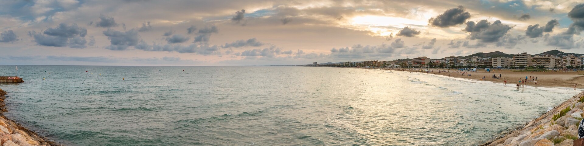 A coastal cityscape with a beach, rocky shoreline, and buildings in the background.