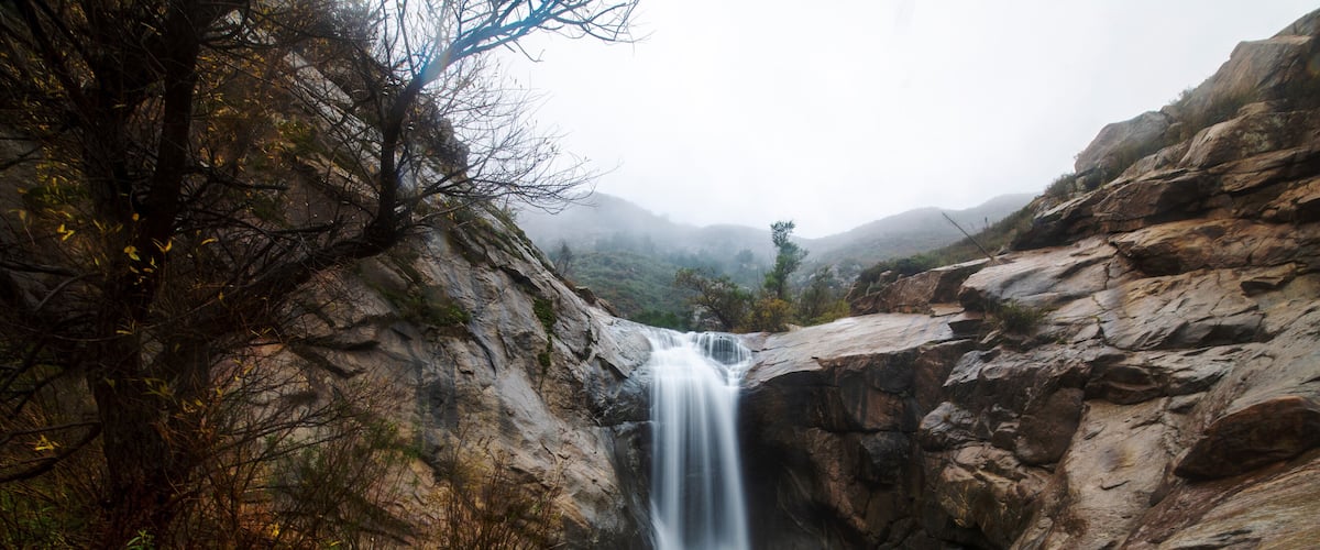 A waterfall cascading down a rocky cliff surrounded by trees and vegetation.