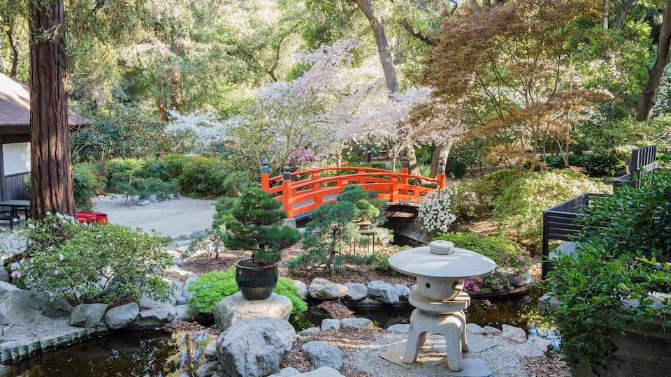 A serene Japanese garden with a red bridge, koi pond, and various plants.