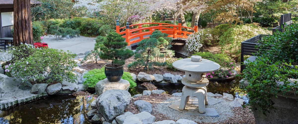 A serene Japanese garden with a red bridge, koi pond, and various plants.