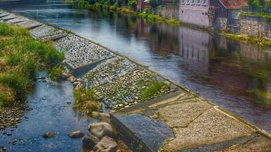 A river flowing through a town with traditional buildings and a mountainous backdrop.