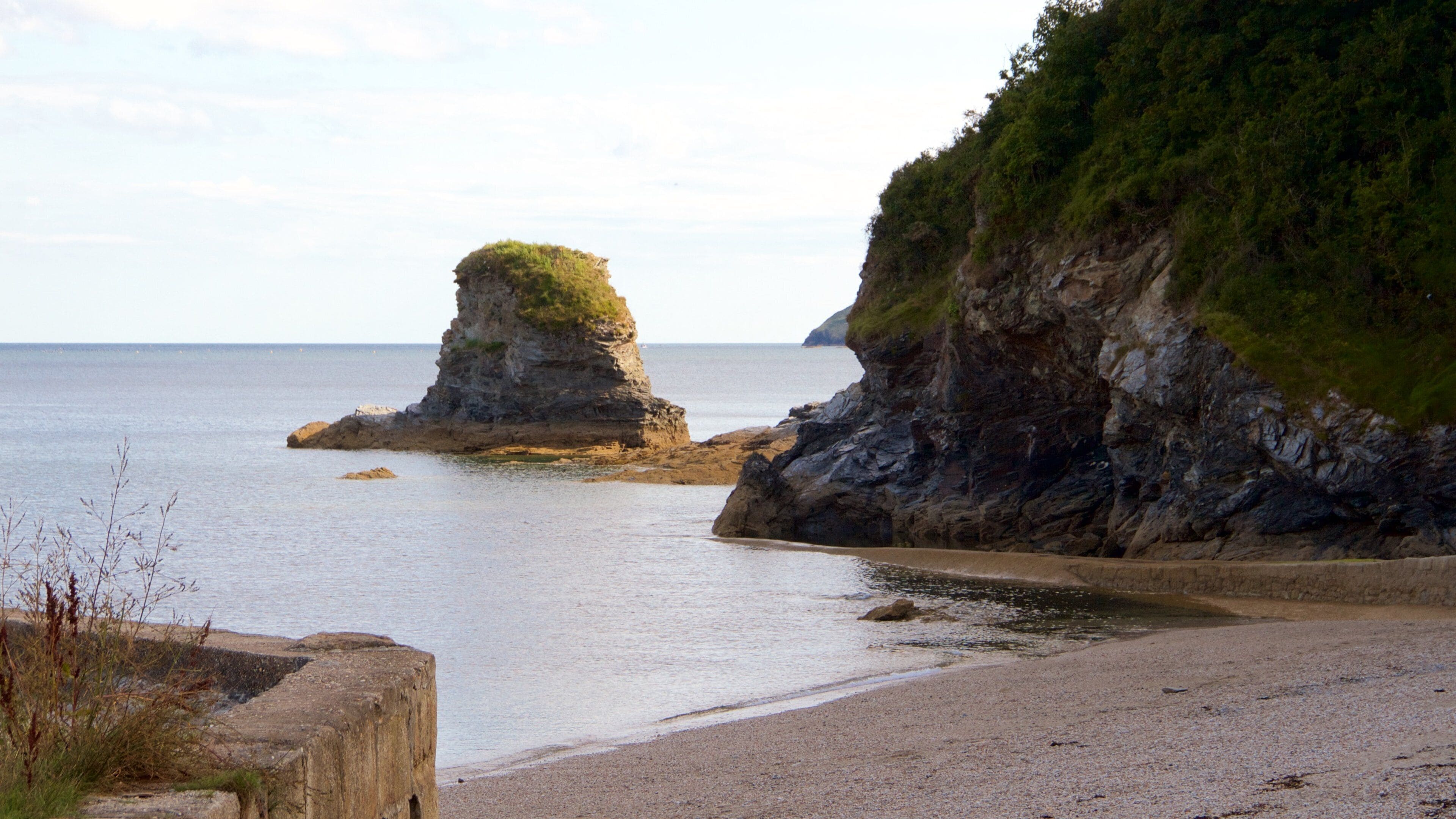 A coastal landscape with a prominent rock formation surrounded by calm sea and a sandy beach.