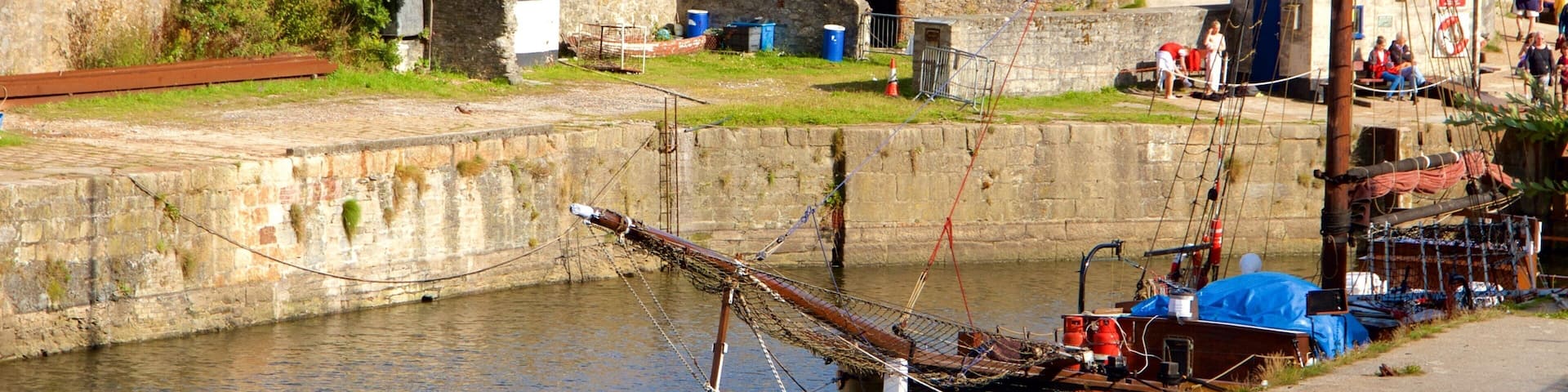A coastal town with a stone wall, a small building, and a large ship.
