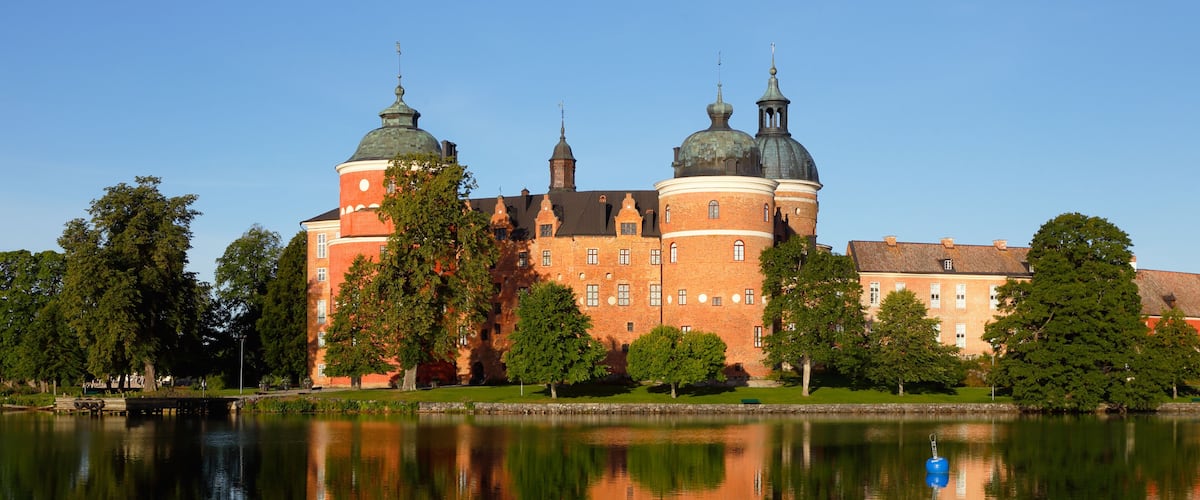 A large brick building with domed towers by a calm lake.