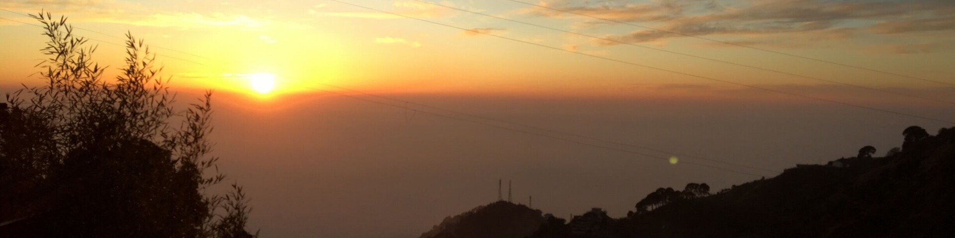 A sunset over a mountainous landscape with silhouettes of trees and a distant power line.