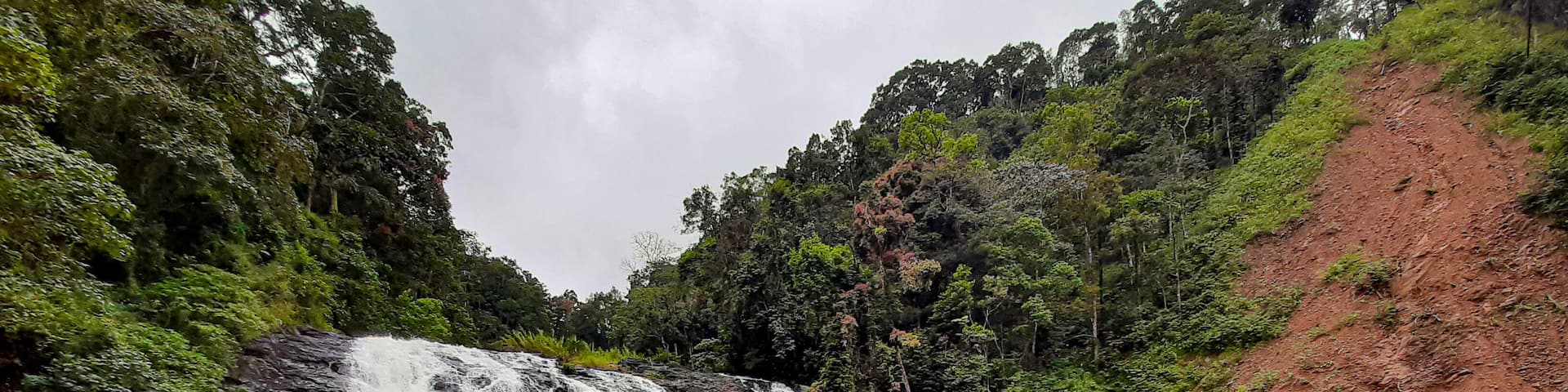 A waterfall cascading into a river surrounded by lush greenery and a red hillside.