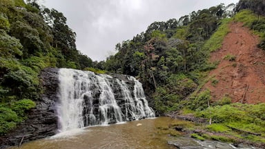 Uma cascata despenca num rio, rodeada por vegetação exuberante e uma encosta vermelha.