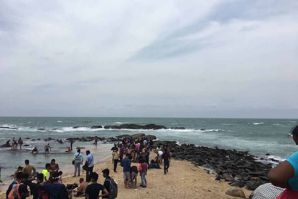 A crowded beach with people near the water and on the sand.