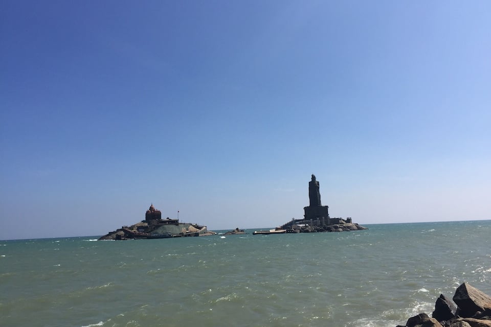 A rocky island with a statue and a building in the sea.