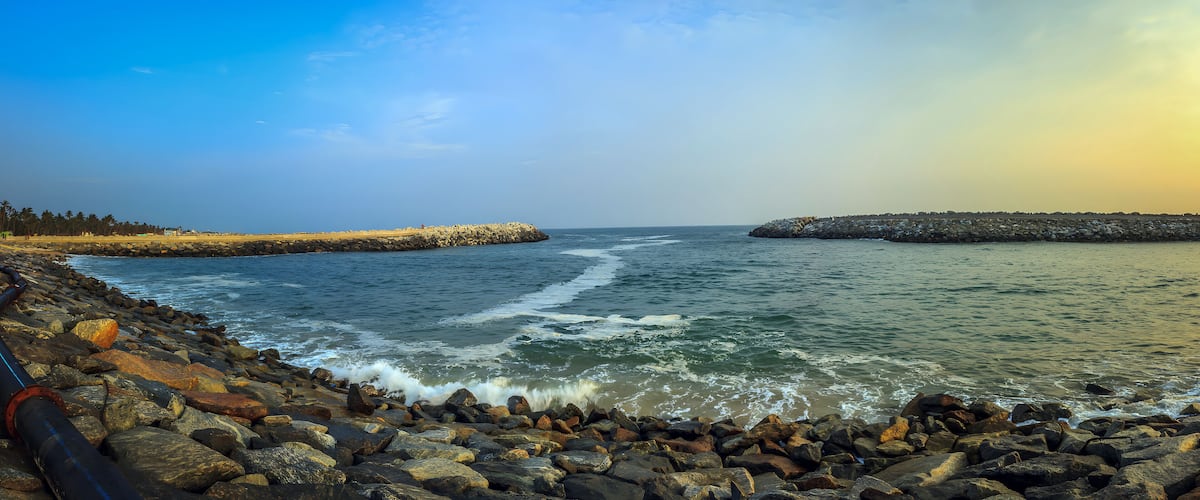 A rocky shoreline with waves crashing against a breakwater and a distant landmass.