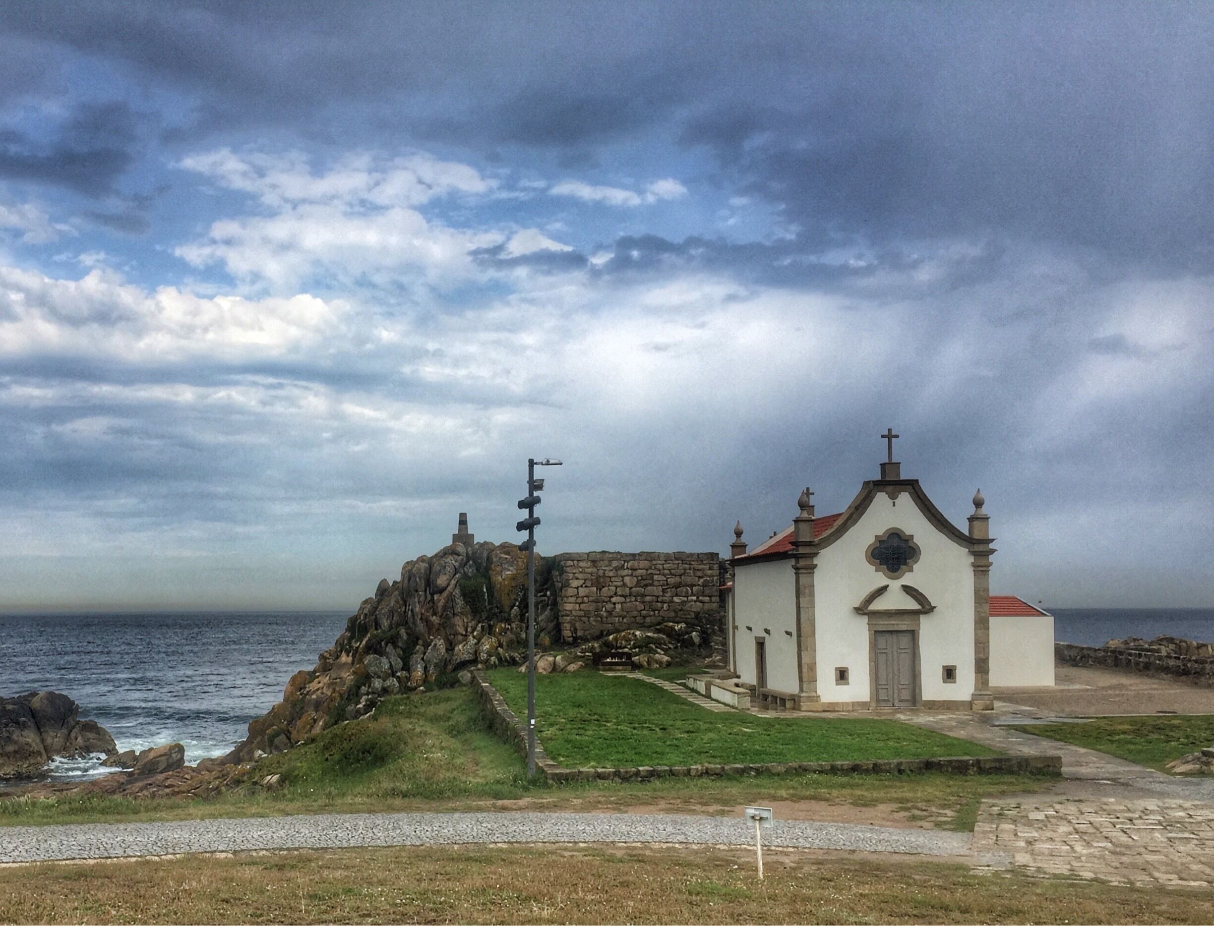 The chapel of Boa Nova is dedicated to St John. The current chapel was designed by the architect Arturo Siza Vieira. This site is said to have housed the original Boa Nova Chapel that dated back as early as 1369. I passed by here as I was hiking the Camino Portugues on a stormy day and loved the Atlantic storm clouds in the background.

#hiking 