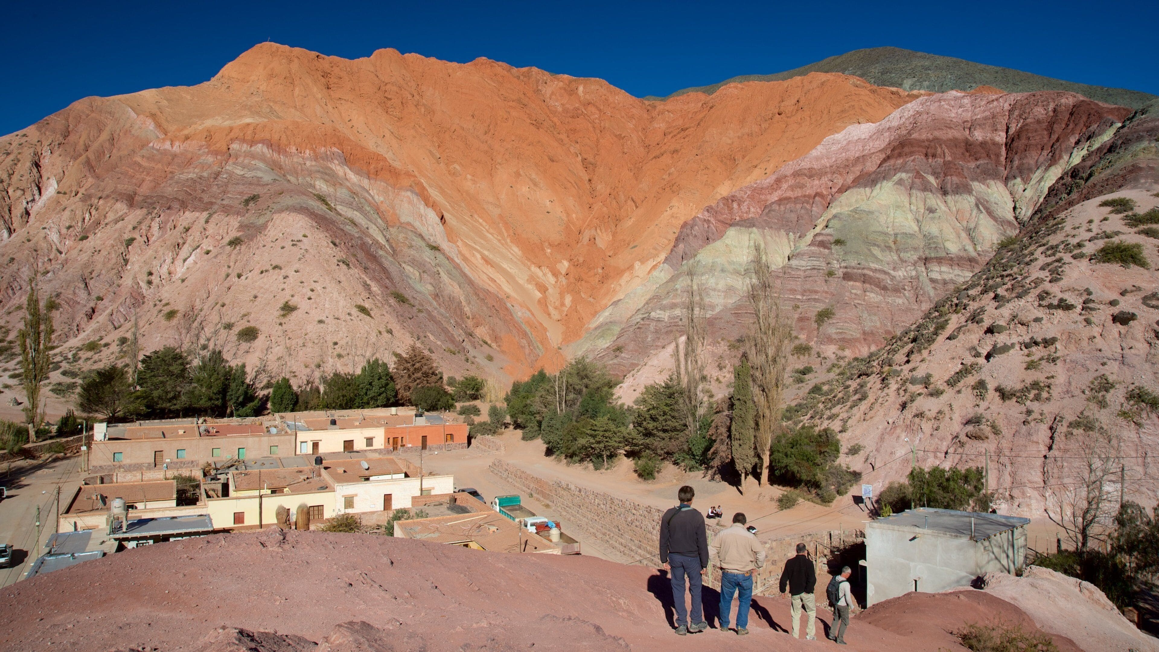 A valley with layered rock formations and a small settlement with buildings and a road.