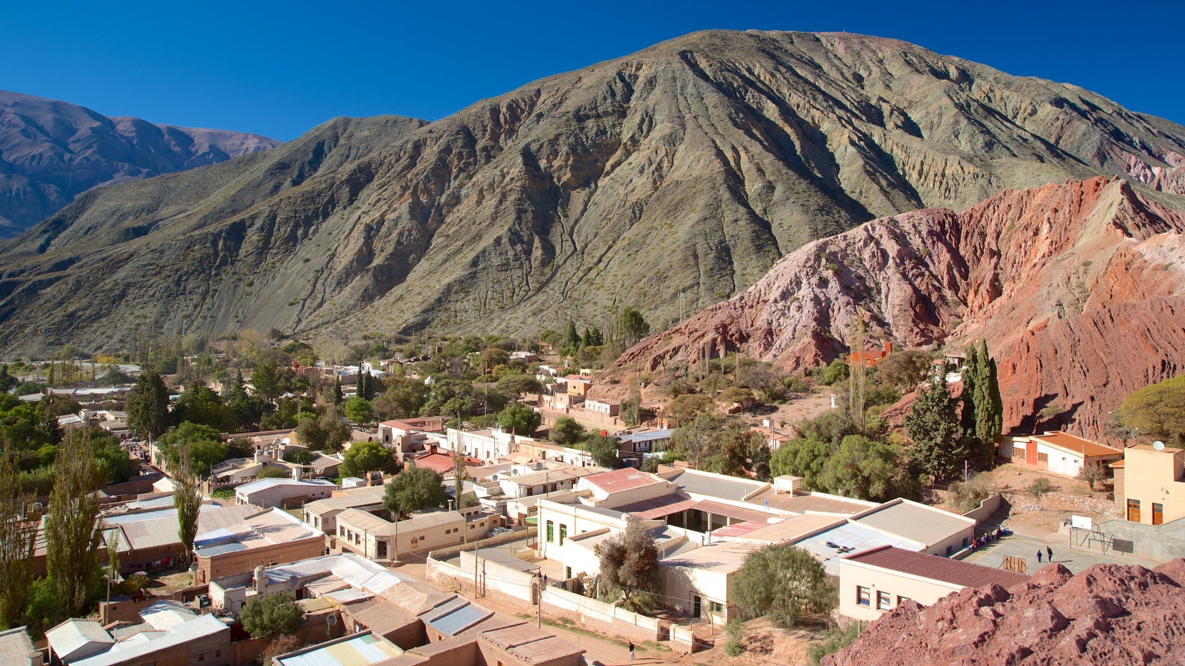 A town nestled against a mountainous backdrop with terraced houses and sparse vegetation.