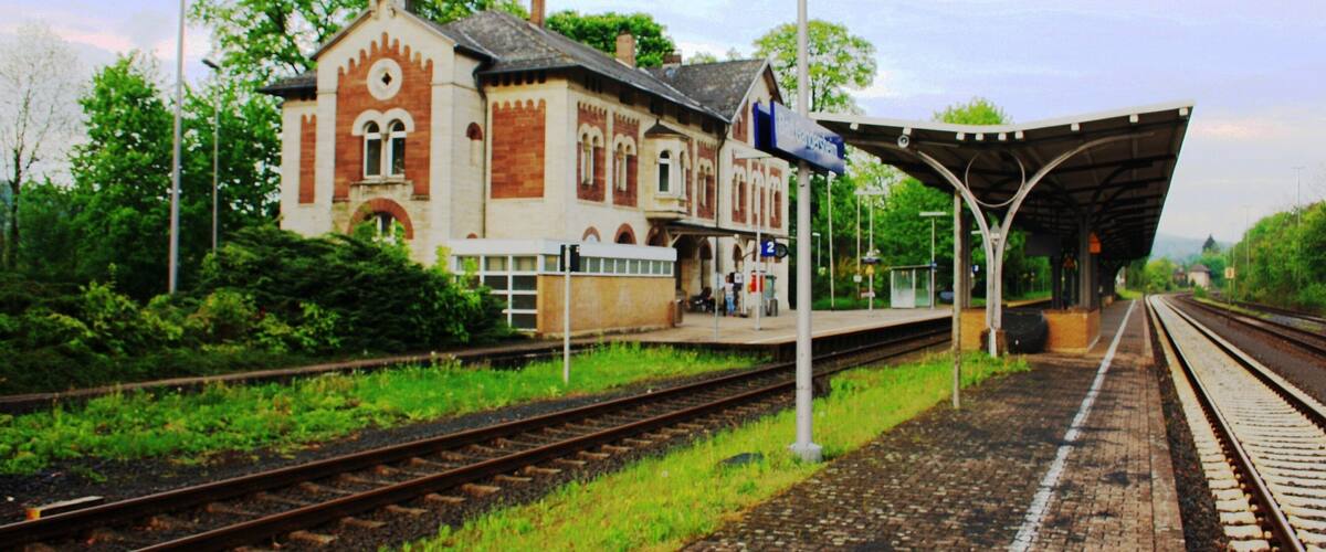 A train station with a red brick building, tracks, and a covered waiting area.