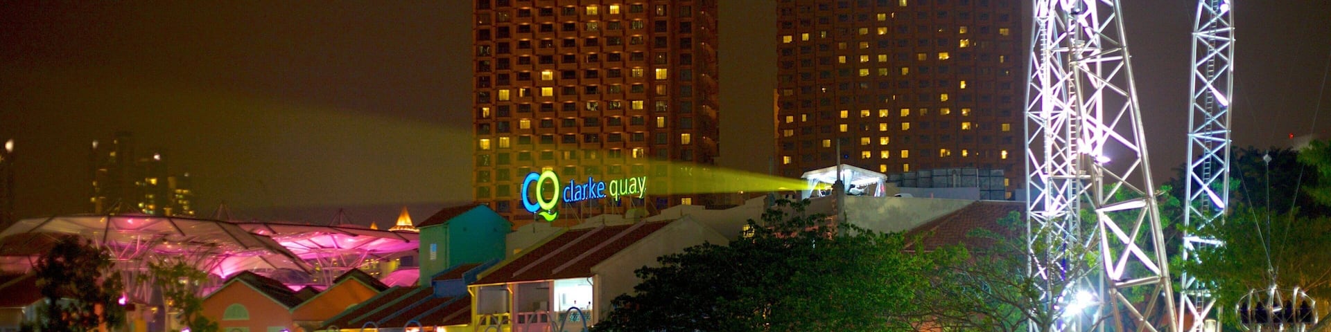 A waterfront with a restaurant, a crane, and illuminated buildings in the background.