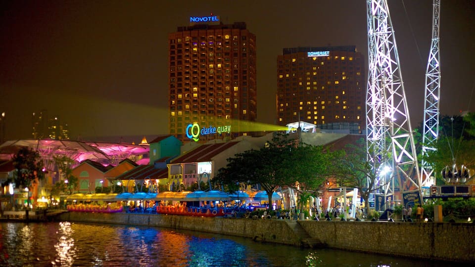 Una orilla con restaurante, una grúa y edificios iluminados al fondo.