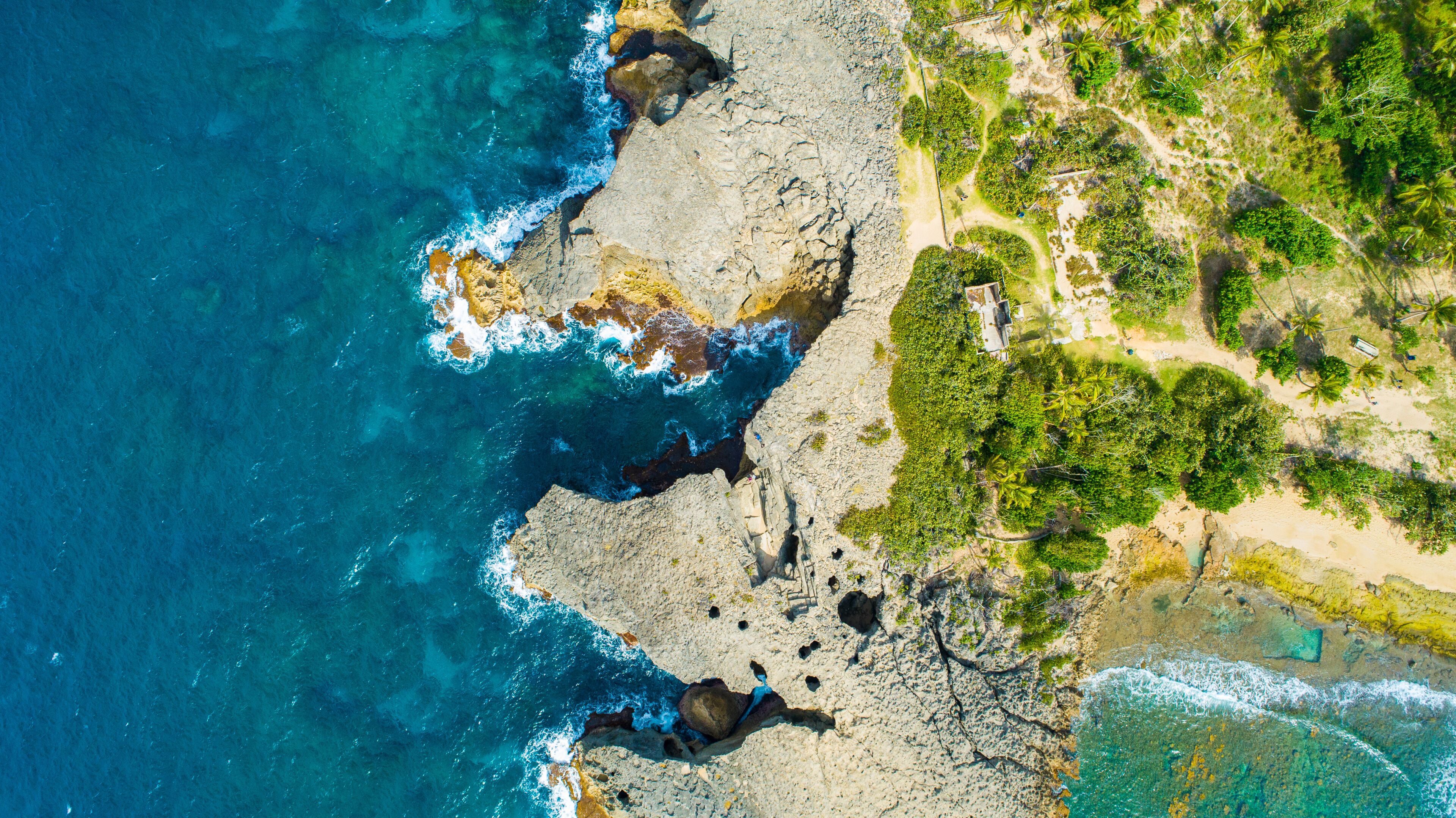 A coastal landscape with rocky cliffs, clear blue waters, and dense greenery.