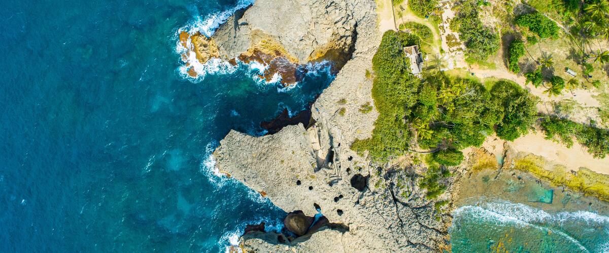 A coastal landscape with rocky cliffs, clear blue waters, and dense greenery.