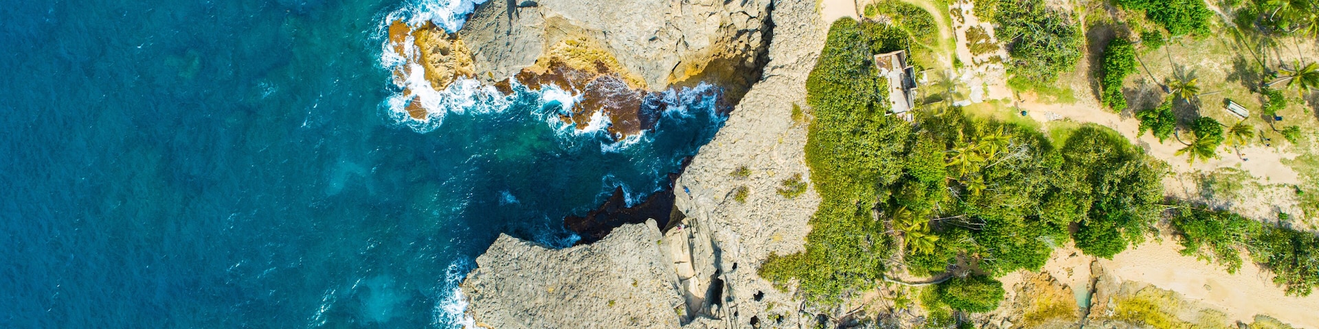 A coastal landscape with rocky cliffs, clear blue waters, and dense greenery.