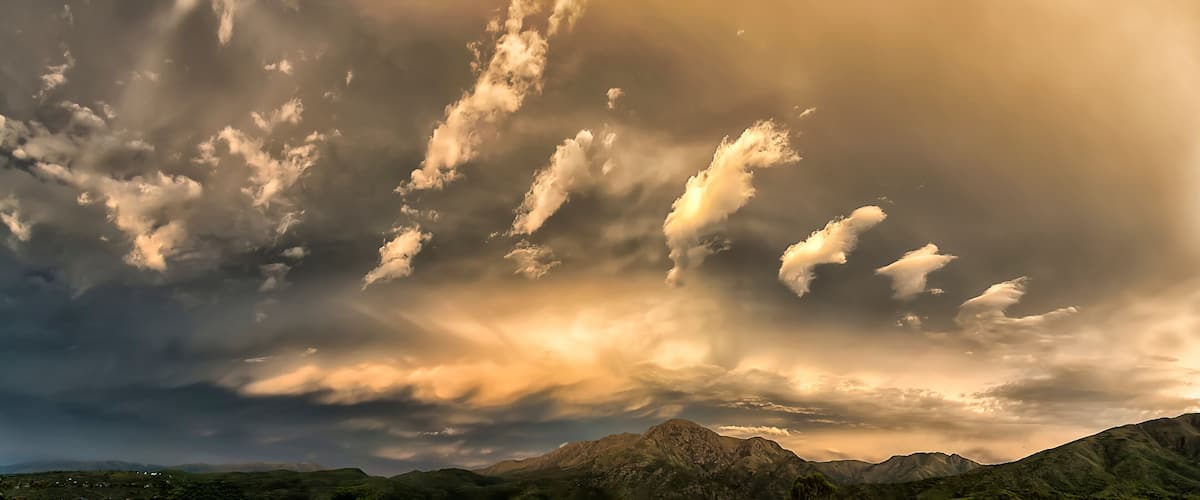 A mountainous landscape with dramatic cloud formations and sunlight filtering through.
