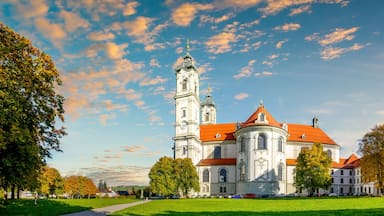 Eine historische Kirche mit einem hohen Glockenturm und einem roten Ziegeldach, umgeben von üppigen grünen Bäumen und einem klaren Himmel.