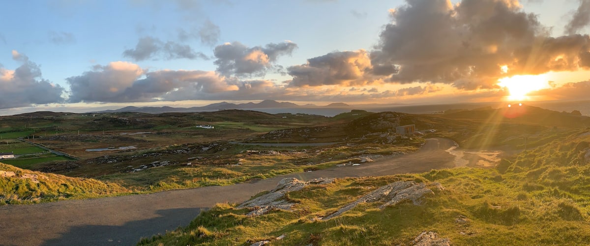 A scenic landscape with rolling hills, a winding road, and a sunset over the horizon.