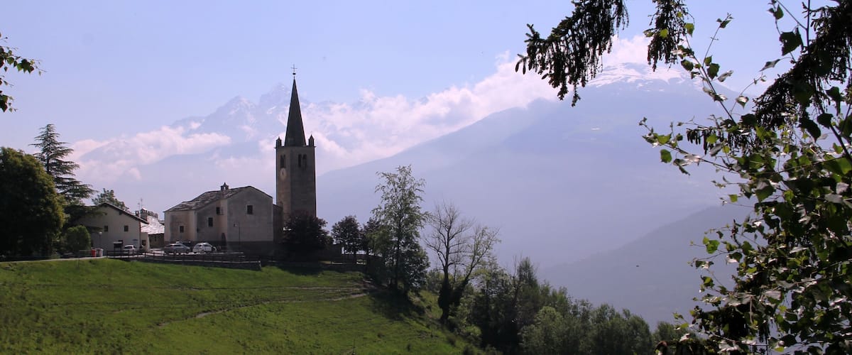 A church with a tall spire, surrounded by trees and a mountain in the background.