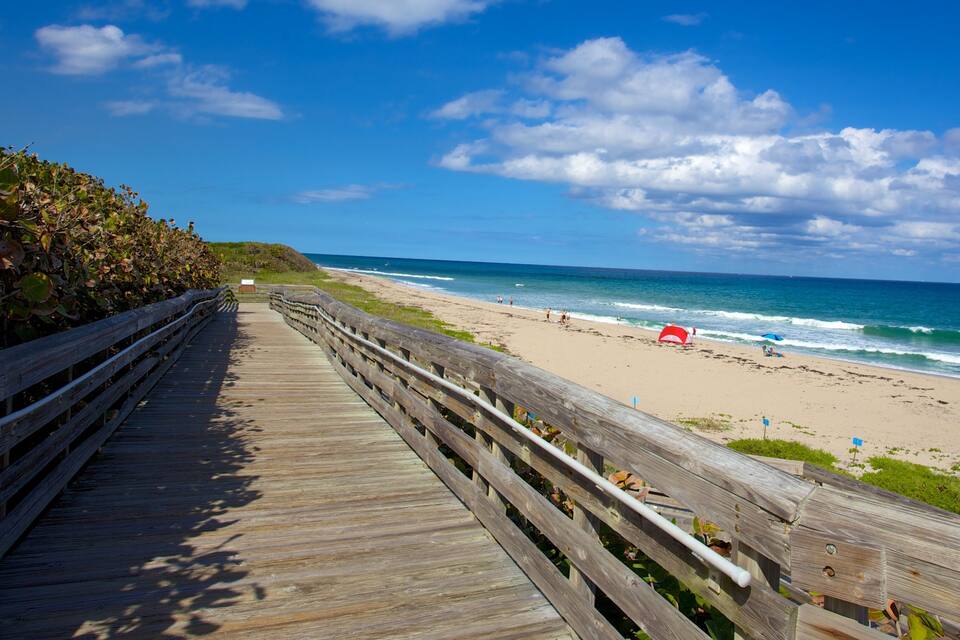 A wooden boardwalk leading to a beach with people and a red tent.