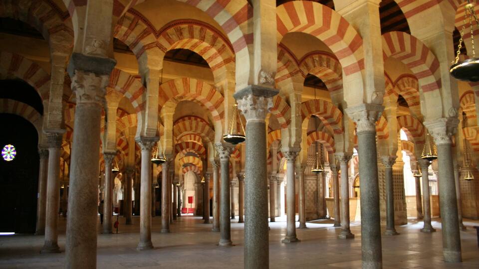 A series of arches with alternating red and white voussoirs, supported by columns in a historic building.