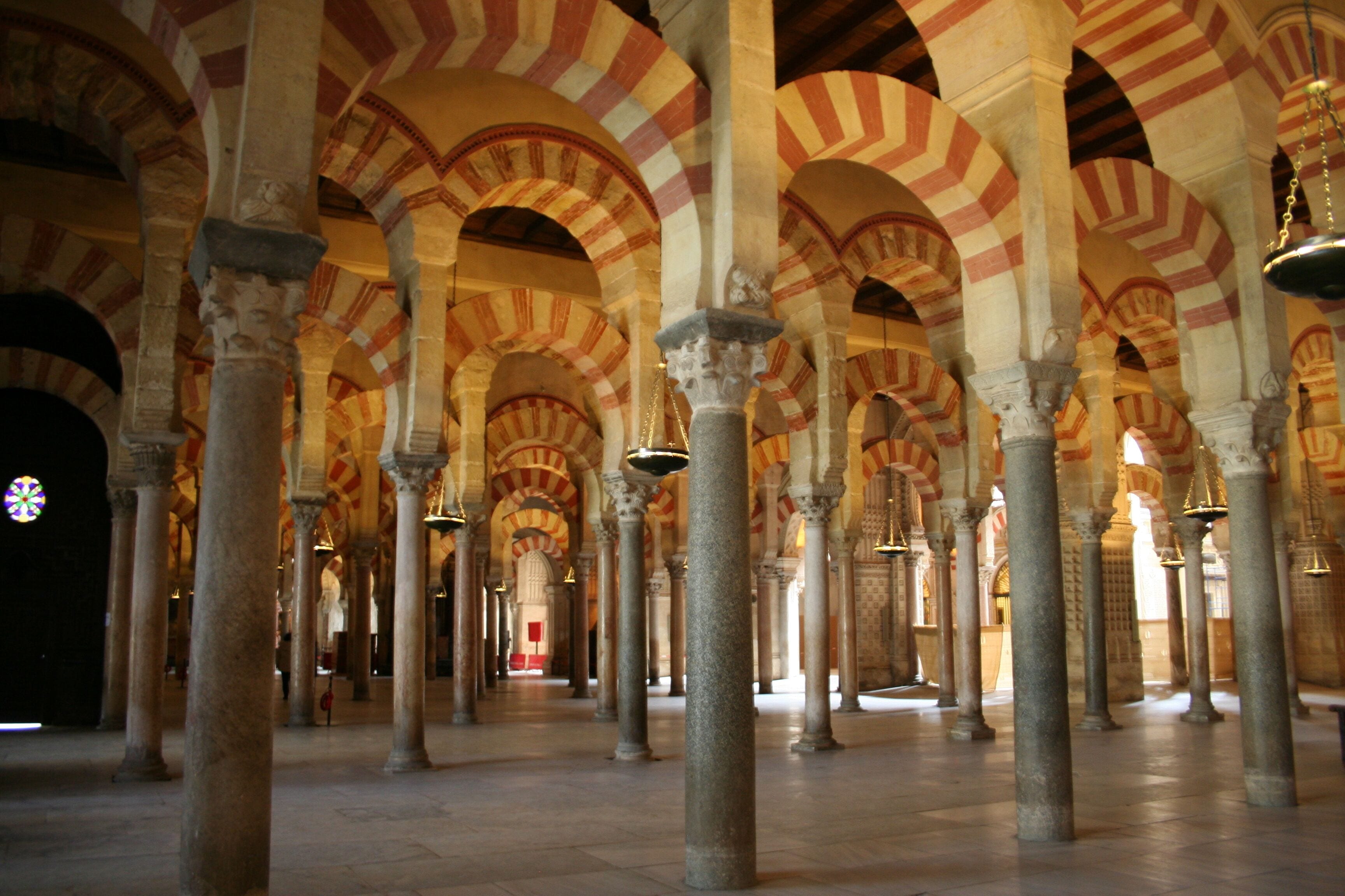 A series of arches with alternating red and white voussoirs, supported by columns in a historic building.