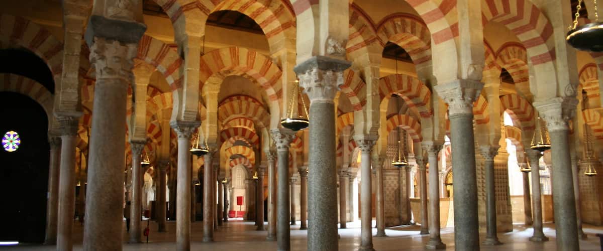 A series of arches with alternating red and white voussoirs, supported by columns in a historic building.