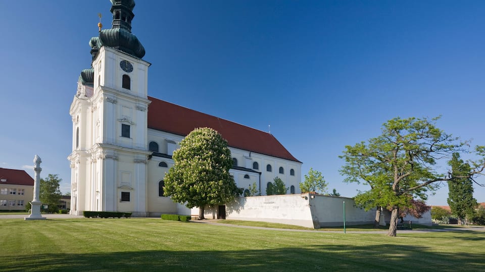 A white church with a red roof and a green dome, surrounded by a well-maintained lawn and trees.