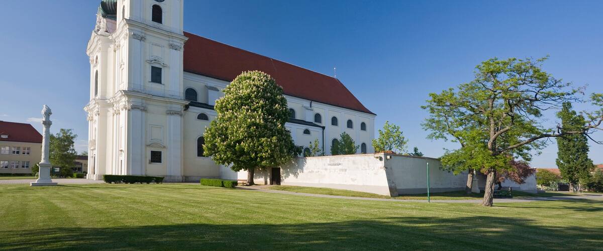 A white church with a red roof and a green dome, surrounded by a well-maintained lawn and trees.