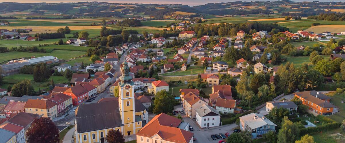 A town with a prominent church tower, surrounded by residential buildings and green fields.
