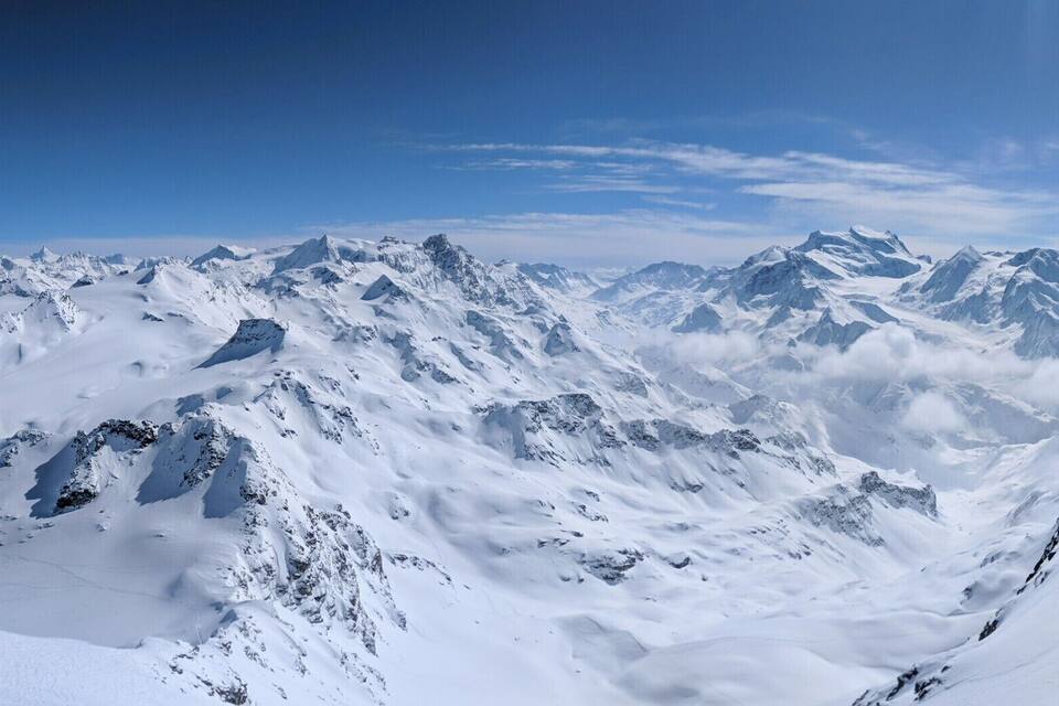 Una cordillera nevada con picos escarpados y valles profundos bajo un cielo azul despejado.