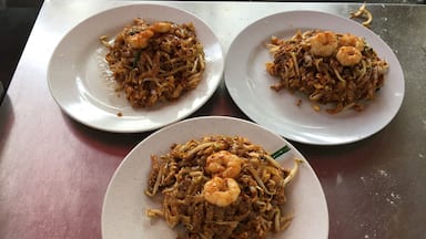 Três pratos de noodles fritos com camarão sobre uma mesa.