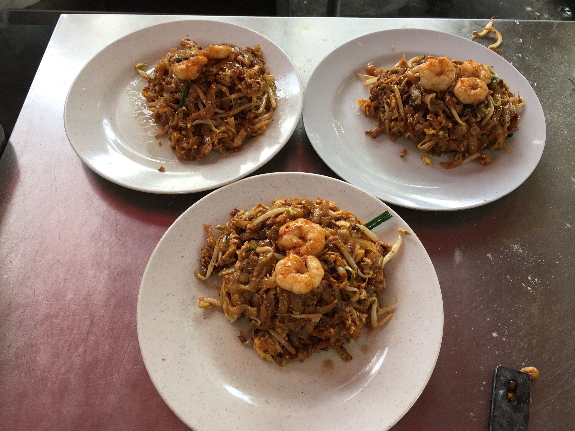 Three plates of stir-fried noodles with shrimp on a table.