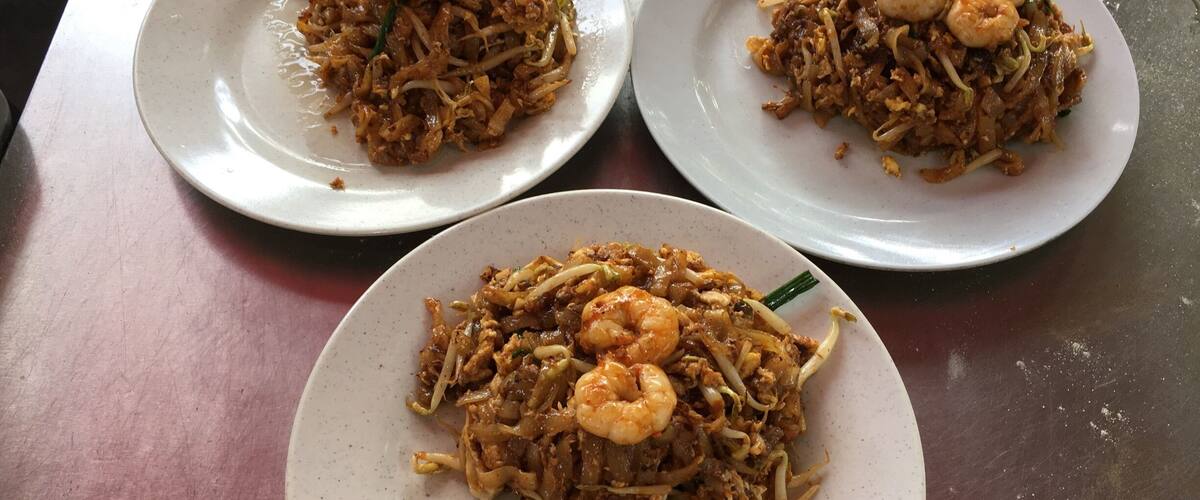Three plates of stir-fried noodles with shrimp on a table.