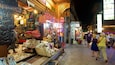 Un mercado nocturno animado con bolsas coloridas, artesanías tradicionales y una variedad de productos expuestos en puestos.