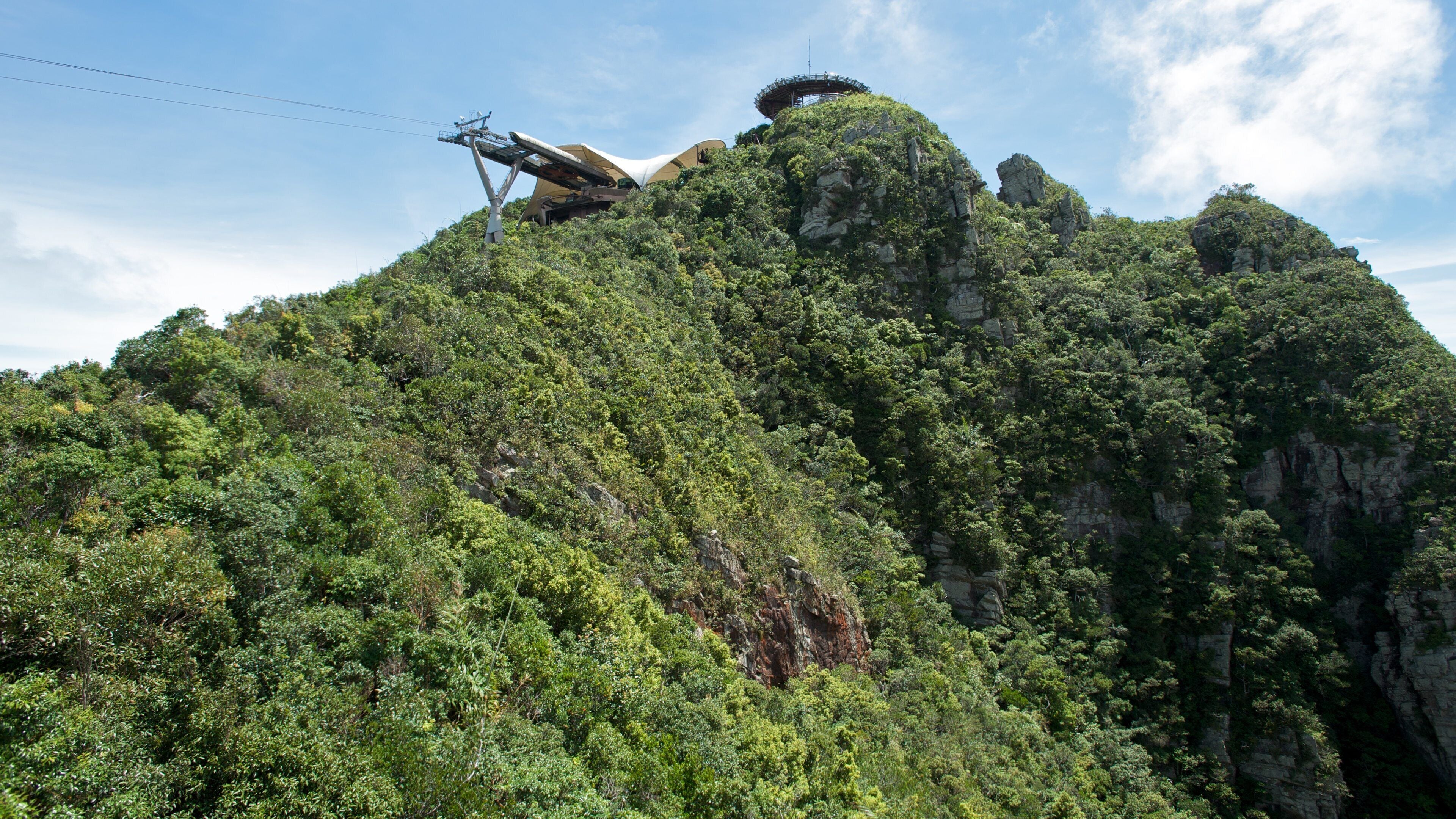 A mountainous landscape with dense green vegetation and a large, uniquely shaped observation tower on top.
