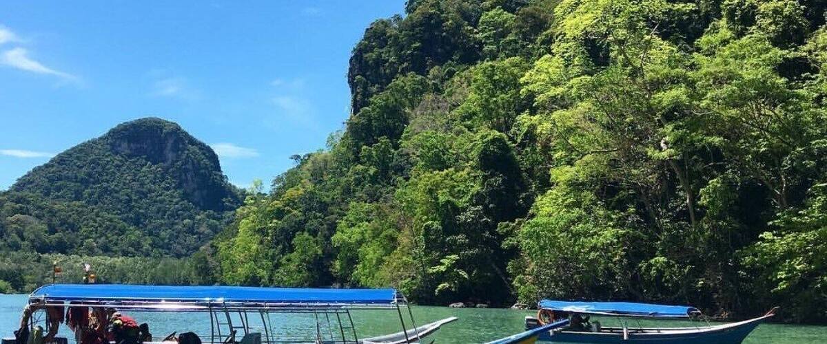 A boat named 'AMIN WAN ENTERPRISE' on calm water surrounded by lush green cliffs.