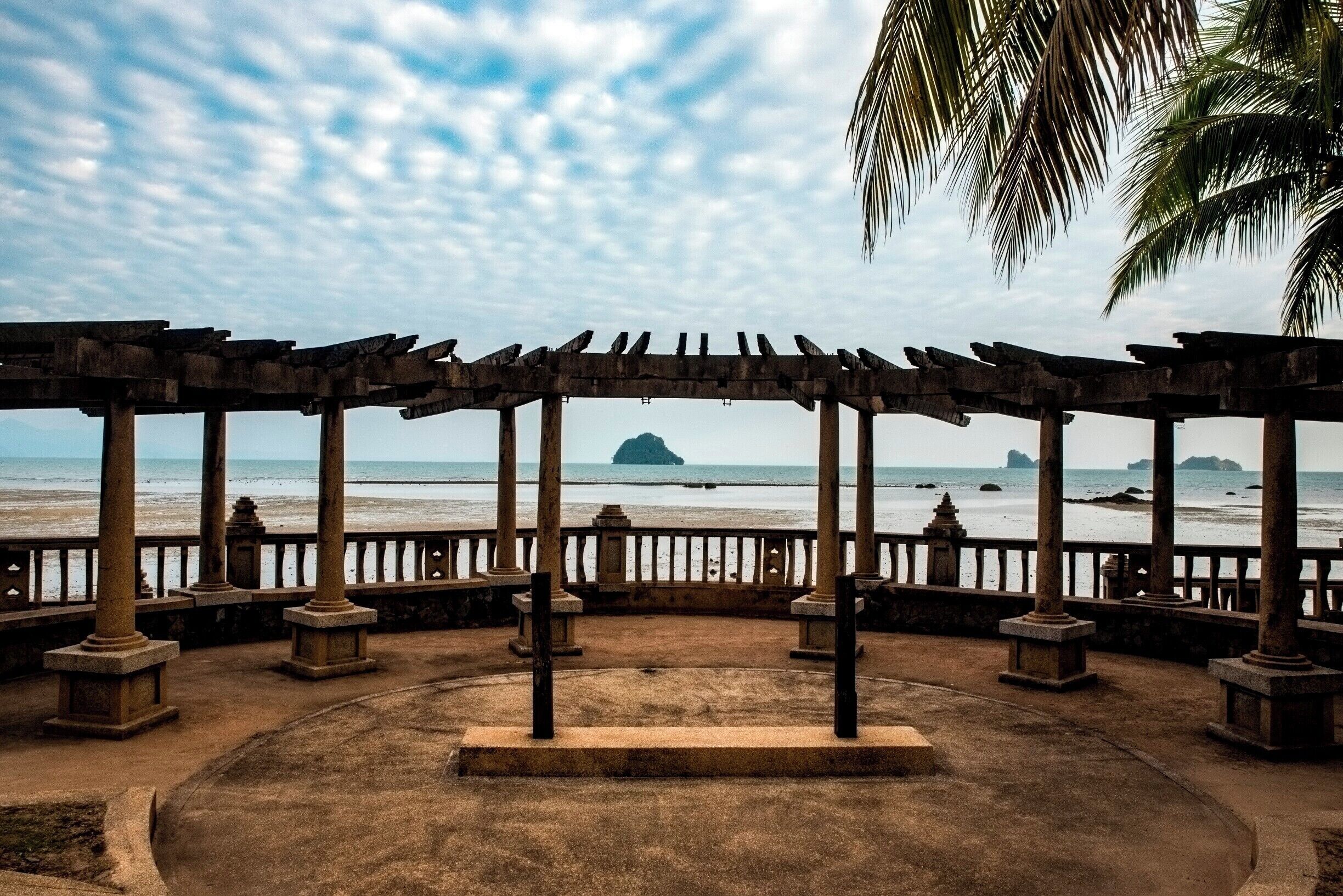 A wooden gazebo with columns overlooking the sea.