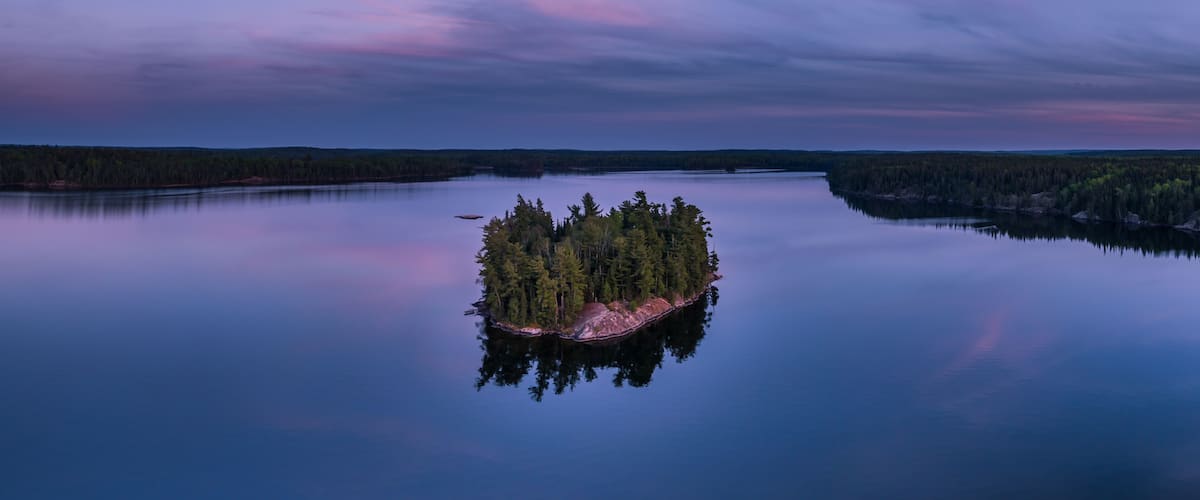 A calm lake with a small island of trees surrounded by forested land.