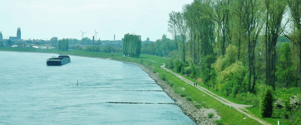 A river with a boat, a path alongside, and wind turbines in the background.