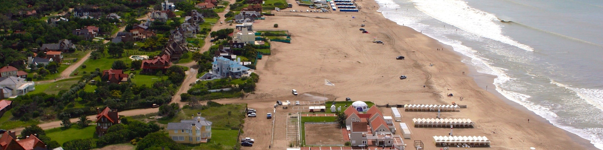An aerial view of a coastal resort with a beach, swimming pool, and beach umbrellas.