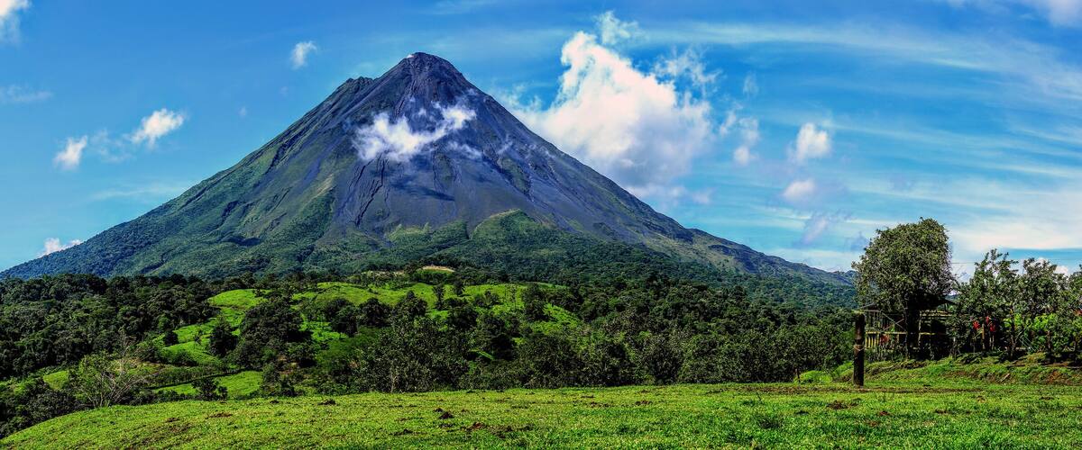 A mountain with a peak, surrounded by lush green fields and trees.